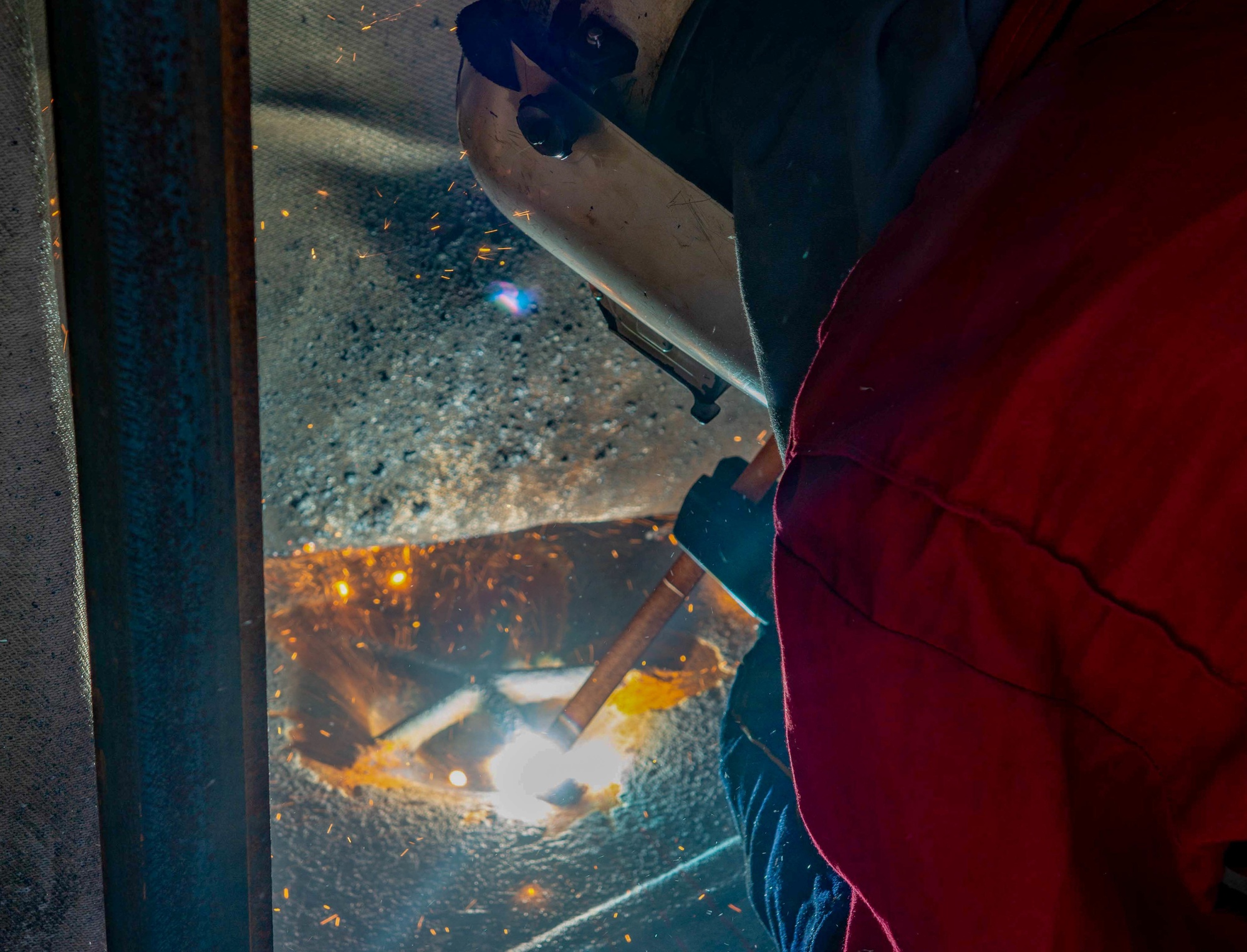 Sailor arc welding on the flight deck of USS John C. Stennis, sparks visible against dusk sky